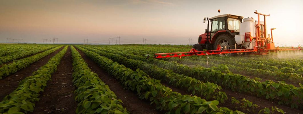 Tractor spraying a field of crops, likely soybeans, with agricultural chemicals. Find Farm Liability Insurance.