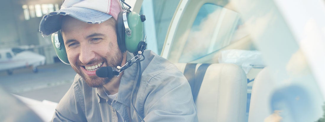 Young pilot sitting in cockpit and enjoying his job. Find Aviation Liability Insurance.