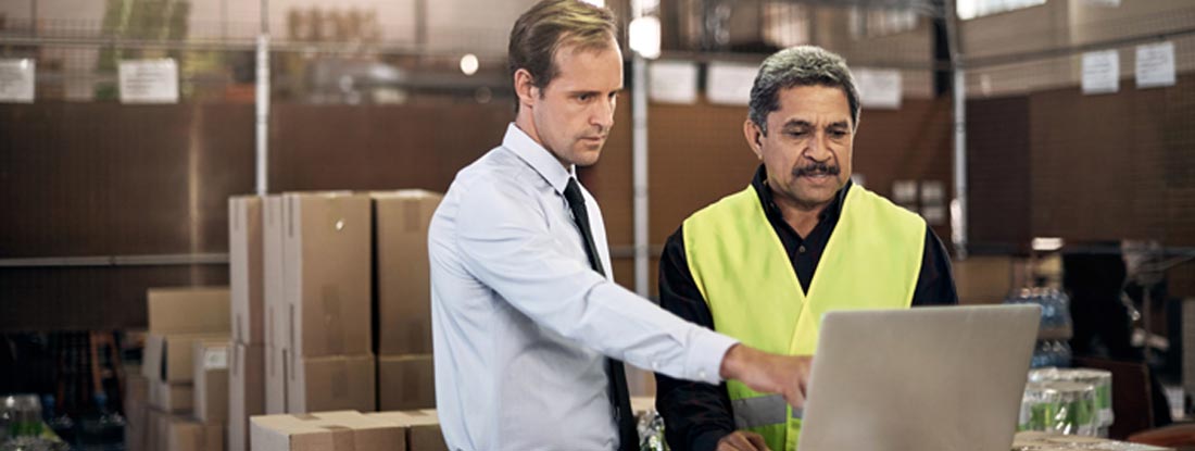 Warehouse worker discussing something on a laptop with his boss in a factory. Workers' Compensation and Employers Liability Exclusion.