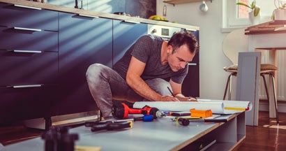 Man checking blueprints while building kitchen cabinets. 6 Major Home Renovations that Impact Your Homeowner’s Insurance Needs.