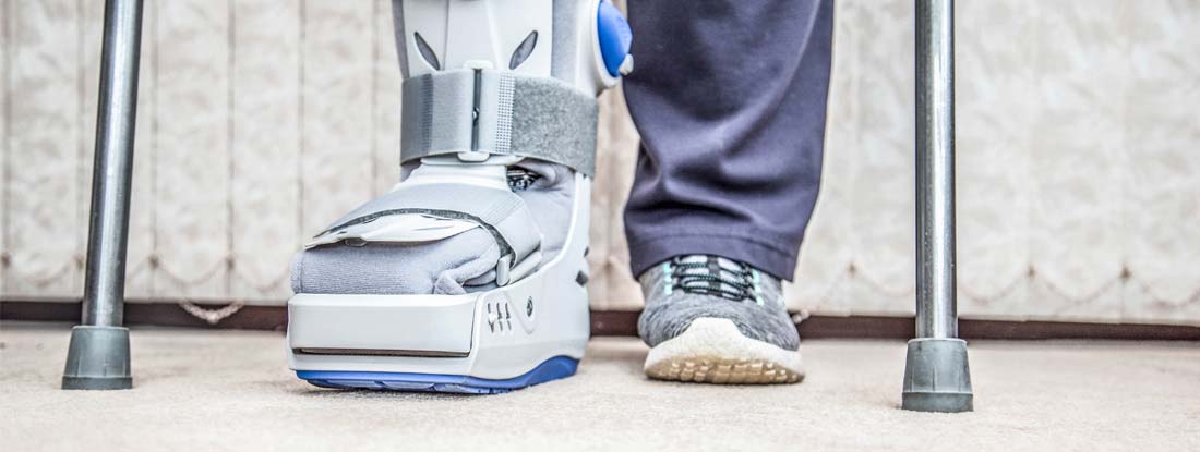 Person using crutches and wearing an ankle-foot orthosis (AFO) boot on their left foot. Disability income insurance riders.