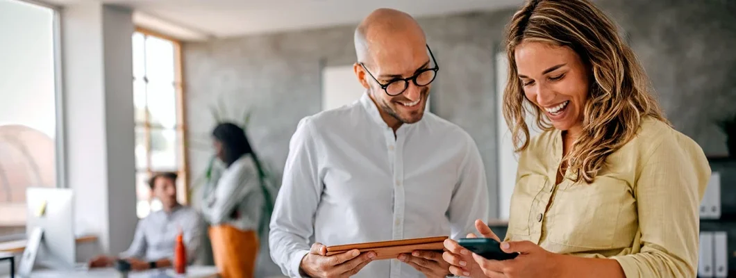 Businesswoman standing with colleague looking at phone in modern office. Business Insurance in Lake Oswego, Oregon.