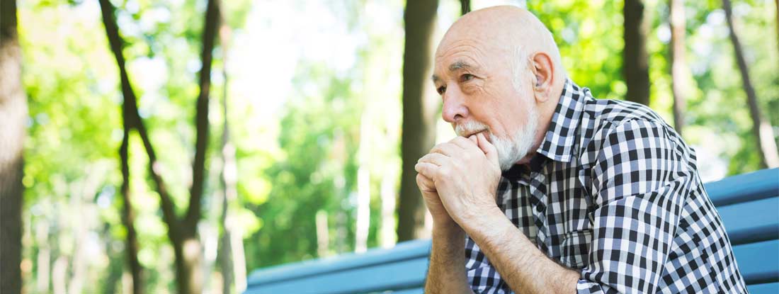 Mature man with a white beard sits alone on a park bench. Annuity policy with cash value.