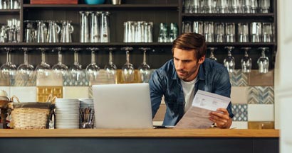 Male cafe owner standing at the counter and paying. Thirteen Business Insurance Pitfalls to Avoid. 