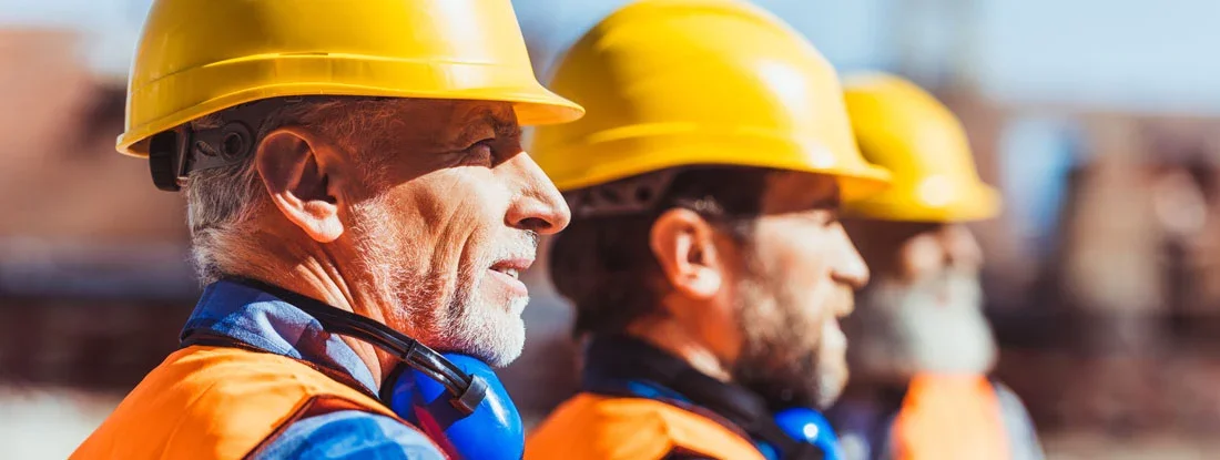 Builders in reflective vests and hardhats standing together at construction site. Find Licensed, Bonded and Insured Business Insurance.