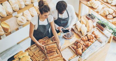 Top view of bakers inside the bakery, holding a digital tablet and arranging the pastries
