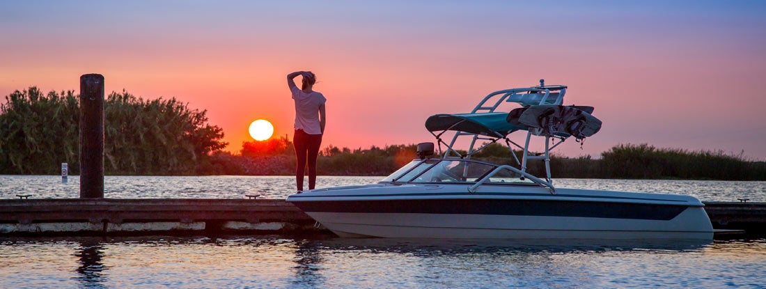 Woman watches the setting summer sun from a dock on a river. Find Mississippi Boat Insurance.