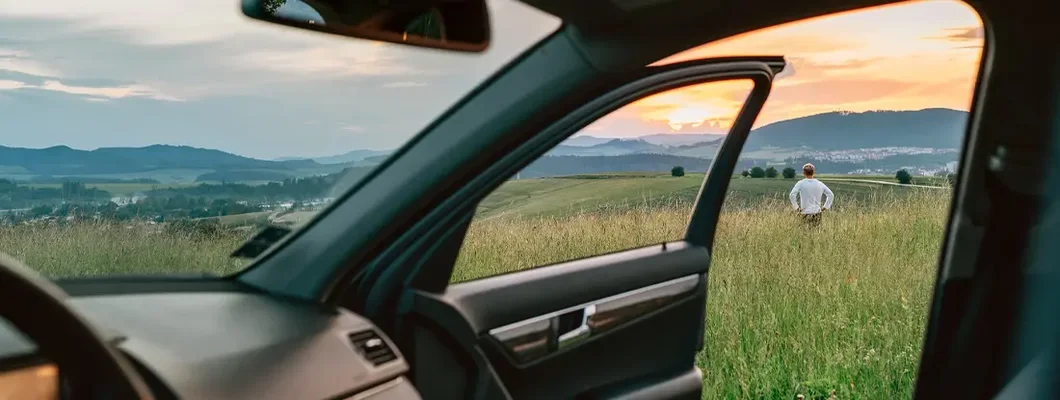 Man standing in high grass and enjoying the sunset sky colors through the open car door view. How to Find the Best Car Insurance in Williston, North Dakota. 