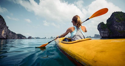 Woman exercising and exploring calm tropical bay by kayak. Find Life Insurance Discounts.