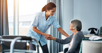 Young nurse helping a senior woman get up from her chair. What does long term care insurance pay for.