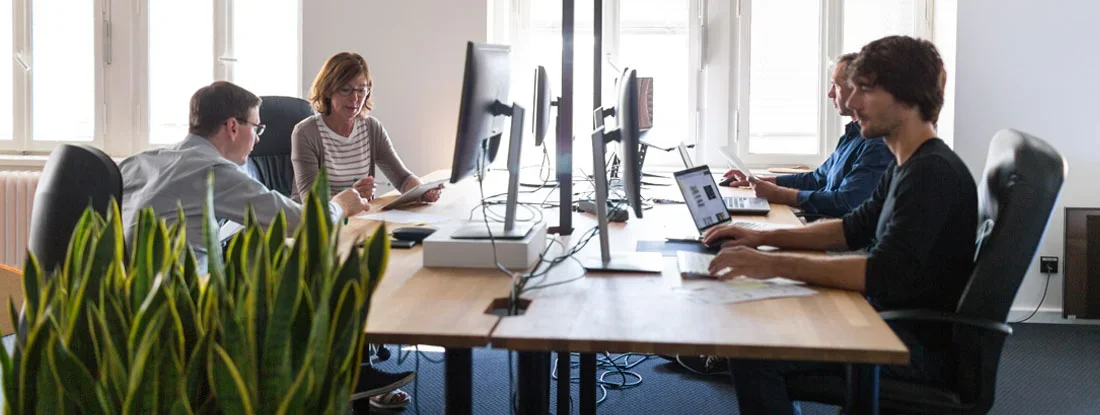 Group of employees is working collaboratively at a large desk. Find Arizona Employment Practices Liability Insurance.