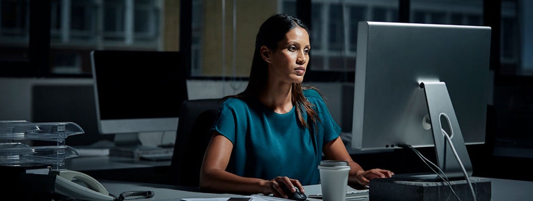 Businesswoman using computer in dark office.  Find Business Cyber Liability Insurance.