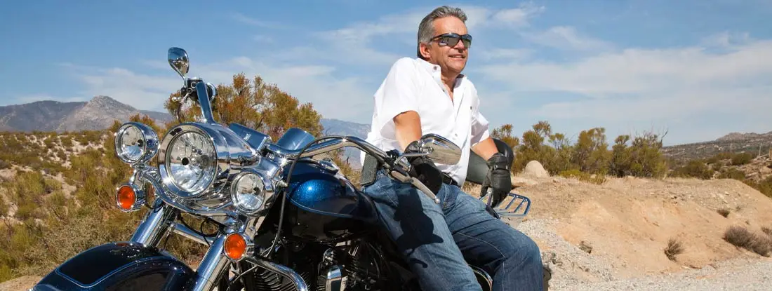 Senior man wearing sunglasses on motorcycle in desert. Find Arizona motorcycle insurance.