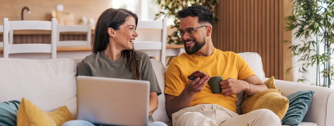 Young couple relaxing on sofa, working and enjoying a cup of coffee. Get Renters Insurance Quotes.