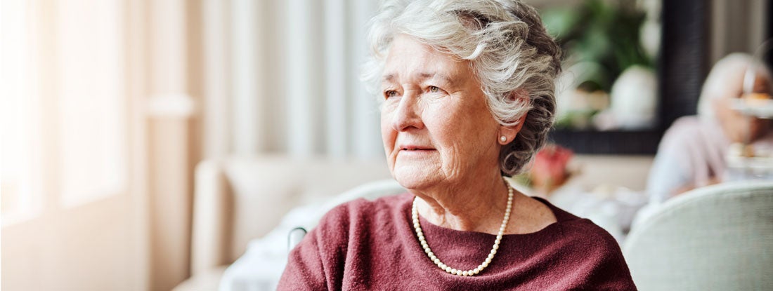 Woman looking thoughtfully out of a window. Traditional long term care companies.