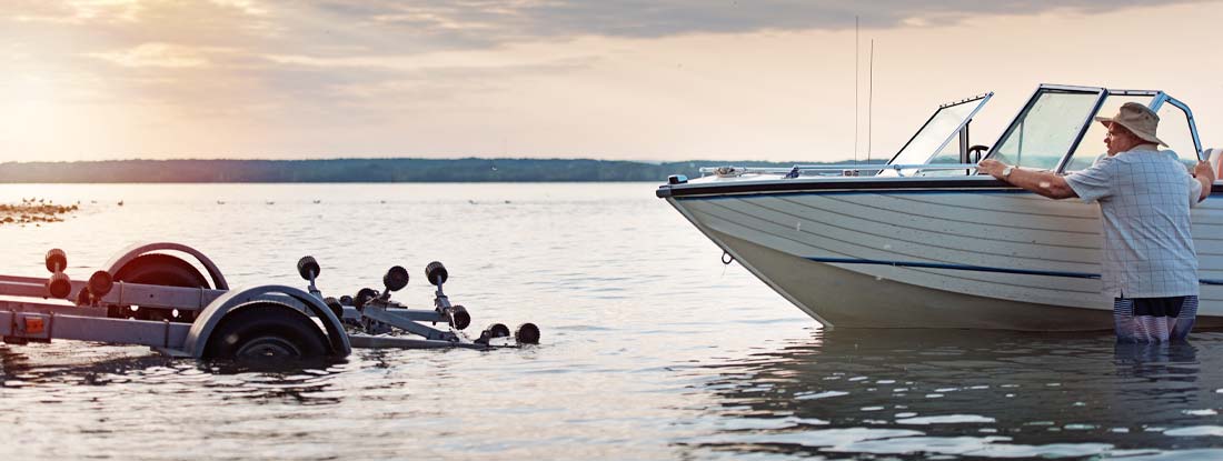 Person maneuvering a boat onto a trailer at a boat launch ramp. Find Trailer Insurance.