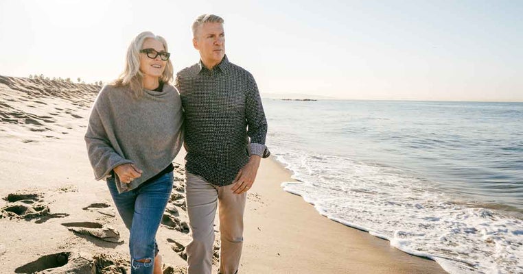 Mature couple walking along beach. Permanent Life Insurance Cost.