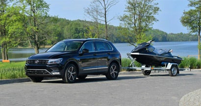 Car and trailer are parked on a paved road beside a lake surrounded by trees. Find Trailer Insurance.