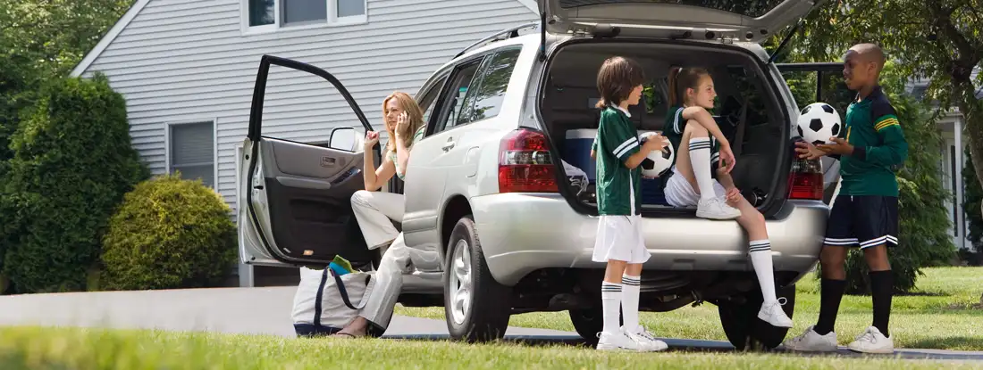 Kids with soccer balls by car in driveway. Umbrella Insurance Discounts.