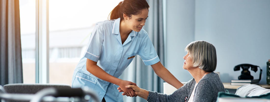 Young nurse helping a senior woman get up from her chair. What does long term care insurance pay for.