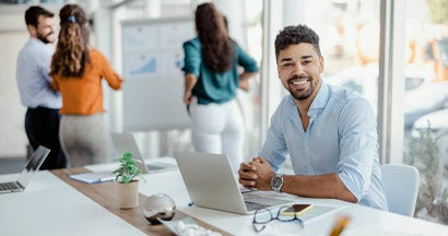Smiling working man looking at camera with colleagues in the background. Find Business Umbrella Insurance. 