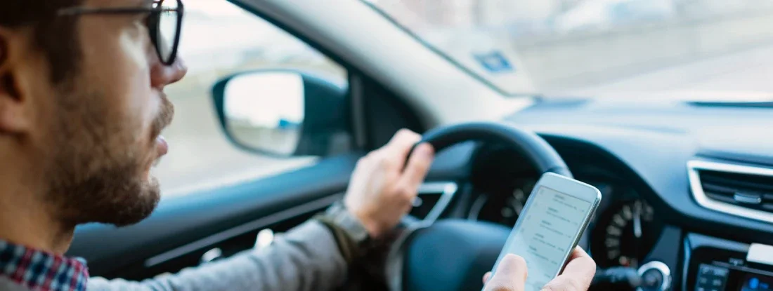 Close up of a businessman using mobile phone while driving. A State-by-State Guide to Distracted Driving Laws and Penalties.