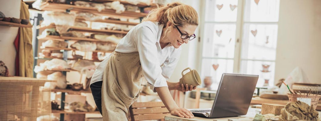 Potter entrepreneur using Shopify on laptop in workshop