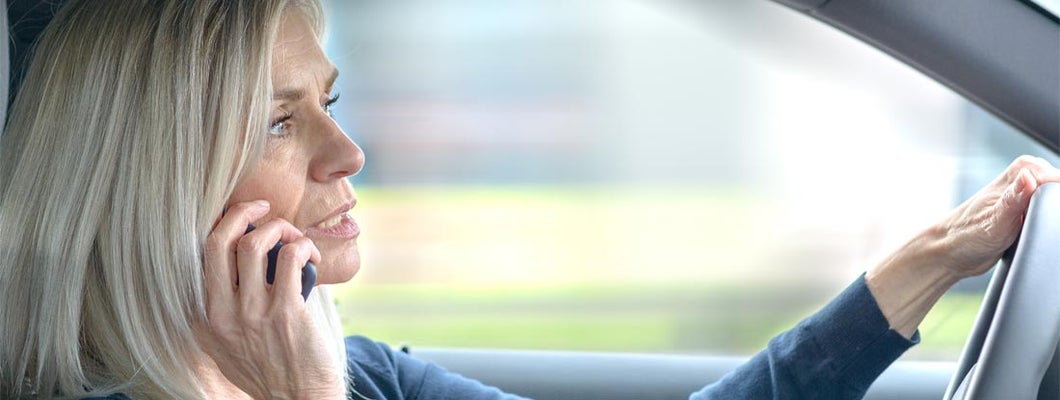 Mature woman talking on her phone in the car as she drives through town. A State-by-State Guide to Distracted Driving Laws and Penalties. 