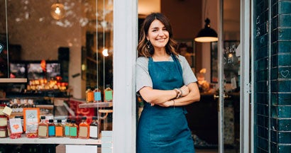 Female owner standing at entrance of deli. Protect your small business in Massachusetts.