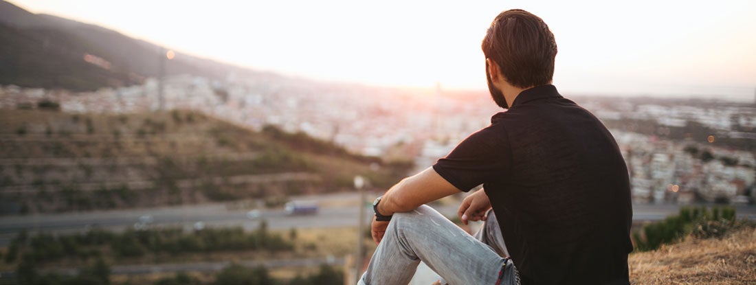 Person sitting and looking out over a city at sunset. Find HIV Life Insurance.
