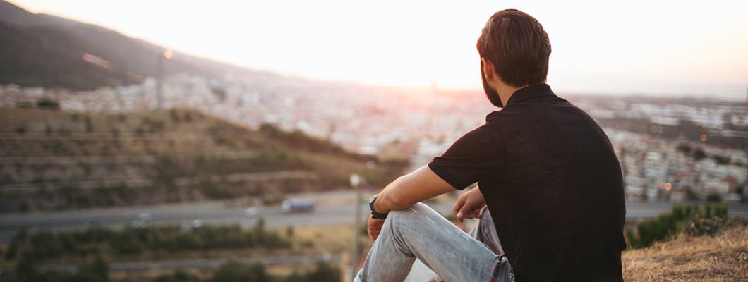 Person sitting and looking out over a city at sunset. Find HIV Life Insurance.