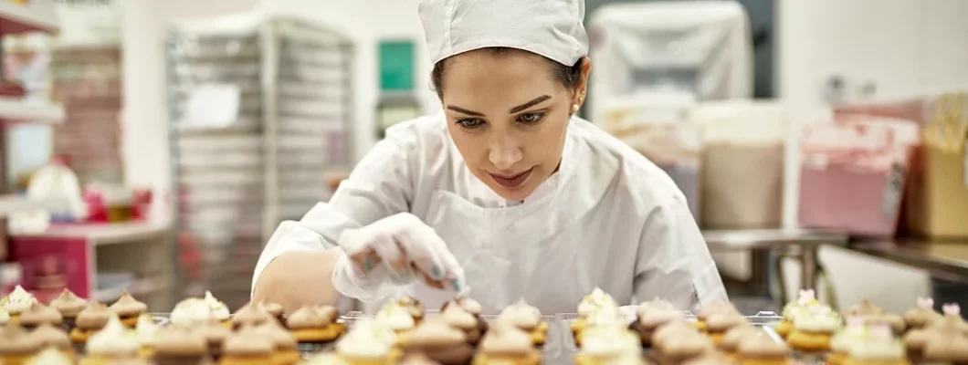 Focused baker decorating fresh batch of cupcakes in commercial kitchen. How to Find the Best Business Insurance in Clayton, Missouri.