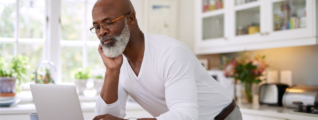 Mature man using a laptop while researching annuities at home. Find Deferred Annuities.