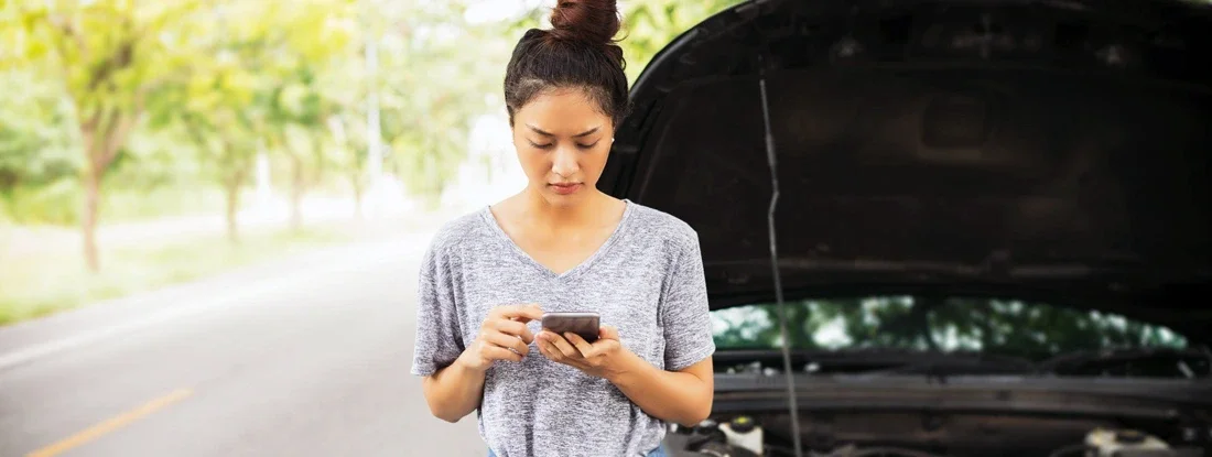 Woman using mobile phone after a car breakdown on street. Should you buy that extended car warranty?