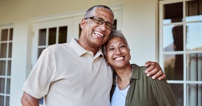 Senior couple smile outside of their home. The difference between landlord and homeowners insurance.