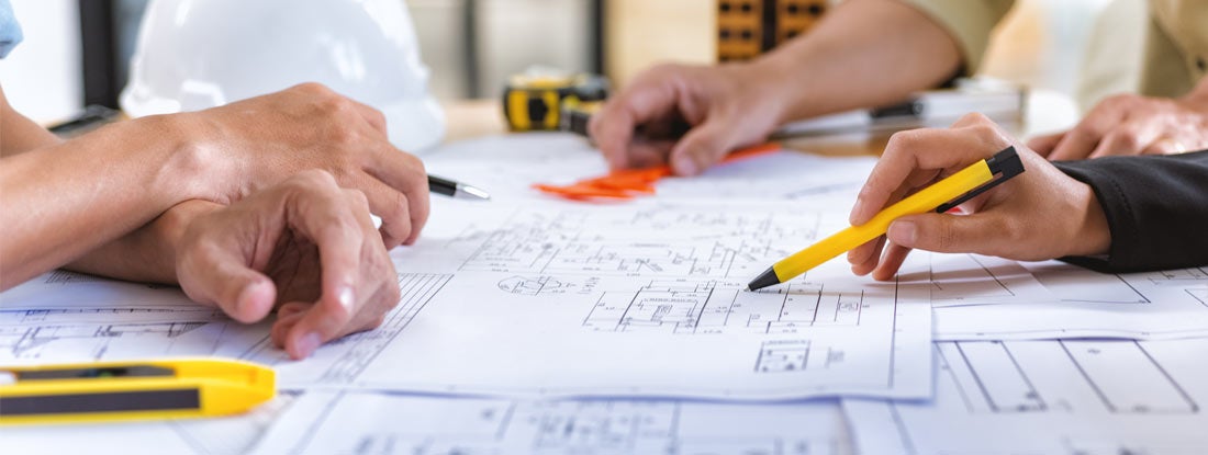 Architect checks construction blueprints on new project with tools at desk in office. Find Architects Insurance.