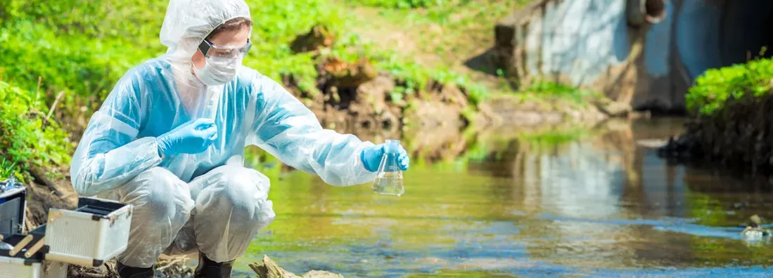 Environmental scientist with a flask takes a sample of water at the site of industrial discharge of water. Find Environmental & Pollution Liability Insurance.