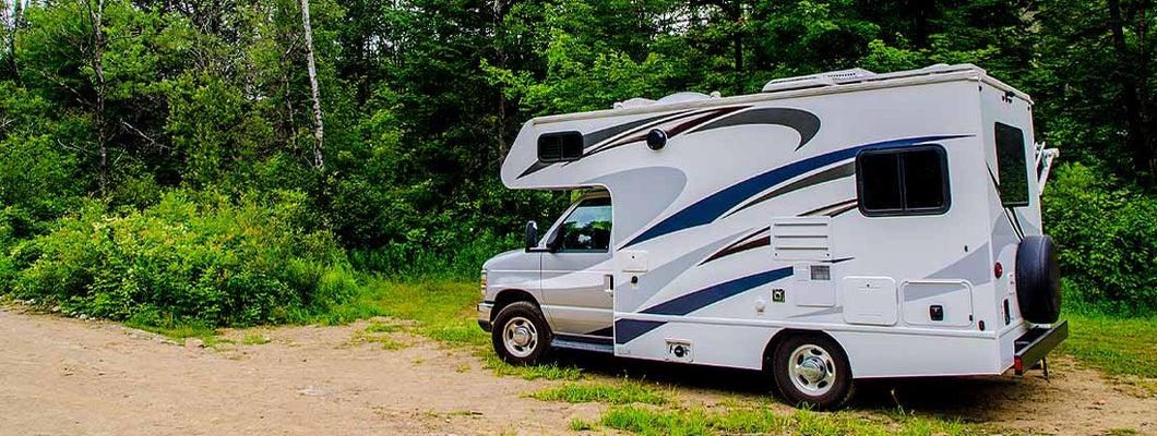 RV parked on sand in forest during day of summer. Find Delaware RV Insurance. 