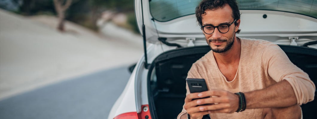 Young man sitting on car trunk. Find El Paso Texas car insurance.