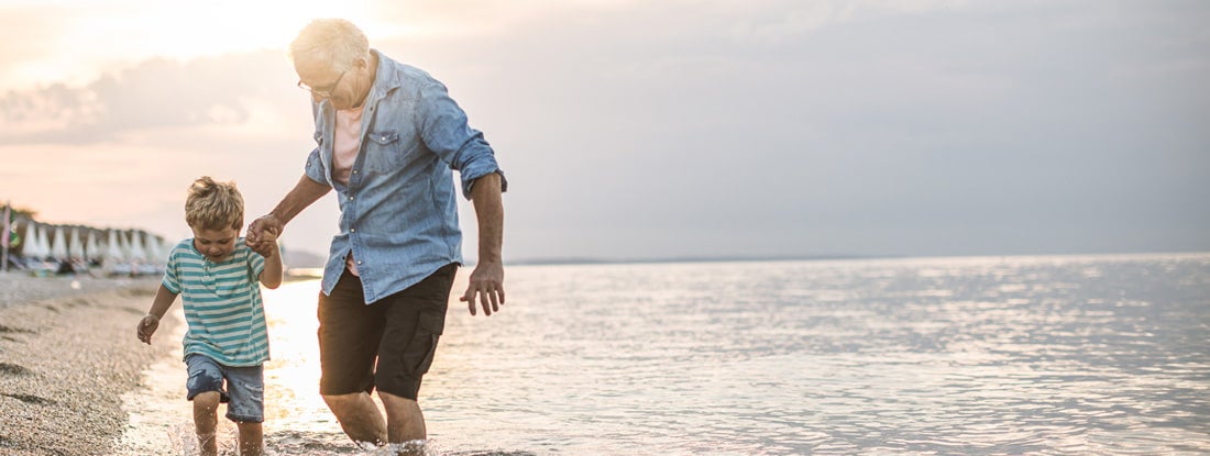 Grandfather and grandson walking at the beach on sunset. Find million dollar life insurance policy.
