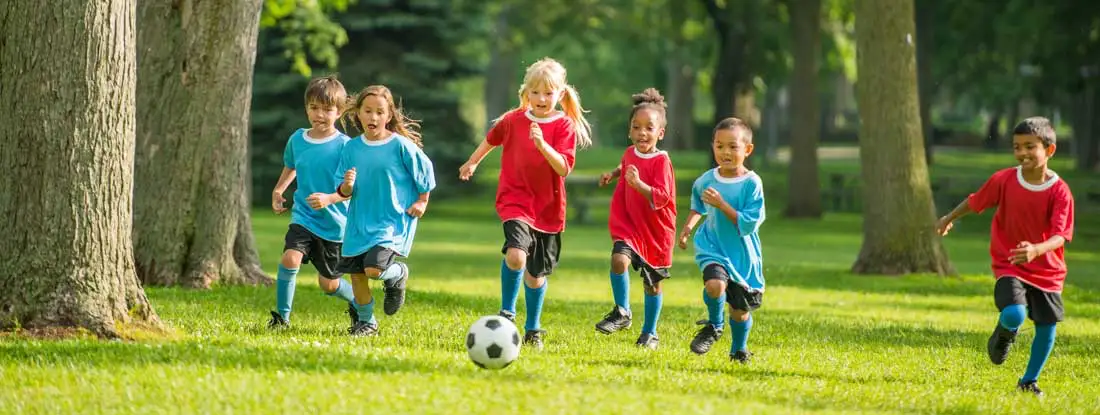 Little kids playing soccer outside at summer sports camp. Find Camp Insurance.