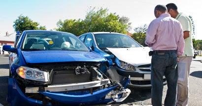 Two men conferring next to car accident. What happens if an at-fault driver doesn't have insurance.