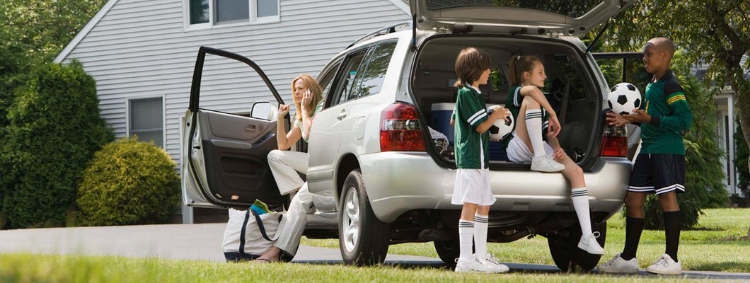 Kids with soccer balls by car in driveway. Umbrella Insurance Discounts.