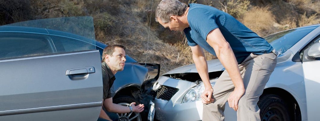 Two men examining damage in car collision. Who's responsible for damages if both drivers were at fault?
