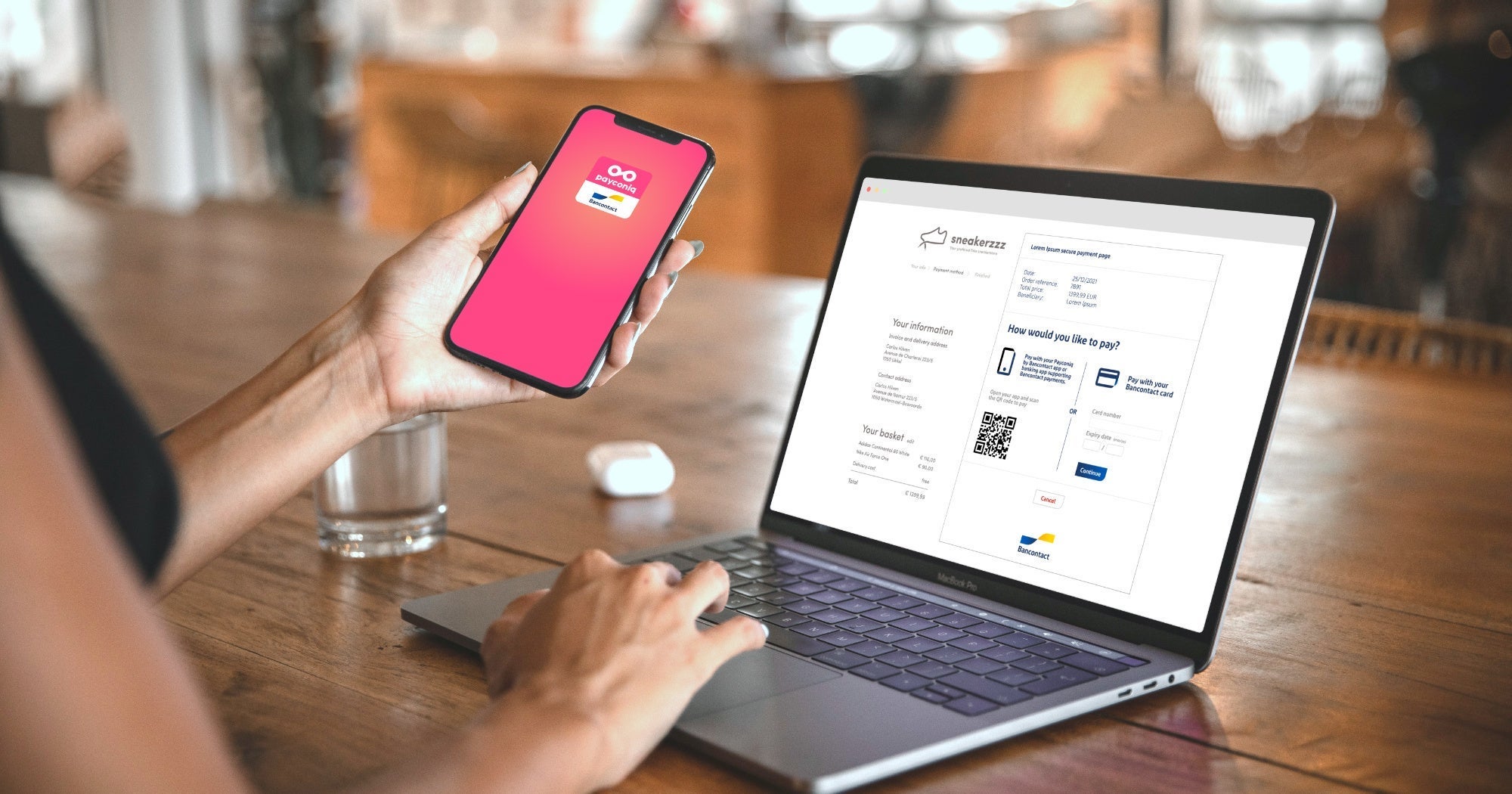 Une femme tenant un smartphone dans sa main se tient devant un ordinateur portable. Sur le smartphone, l'application Payconiq by Bancontact est ouverte, et sur l'ordinateur portable, un code QR Bancontact est visible pour finaliser le paiement.