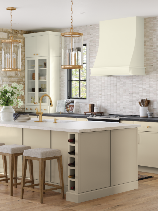 An airy, light-filled kitchen with ivory backsplash, off-white cabinets, and gold statement lighting. 