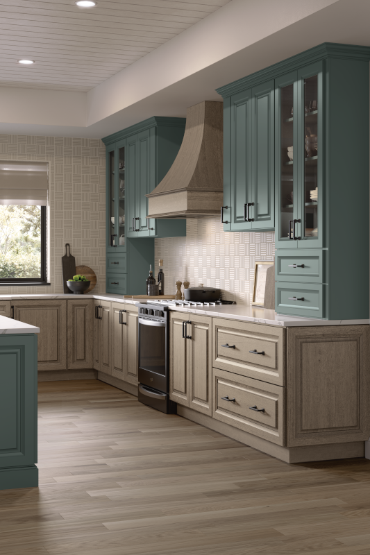 A kitchen with two-tone kitchen cabinets of gray-beige and light blue, light wood floors, and a wood range hood.
