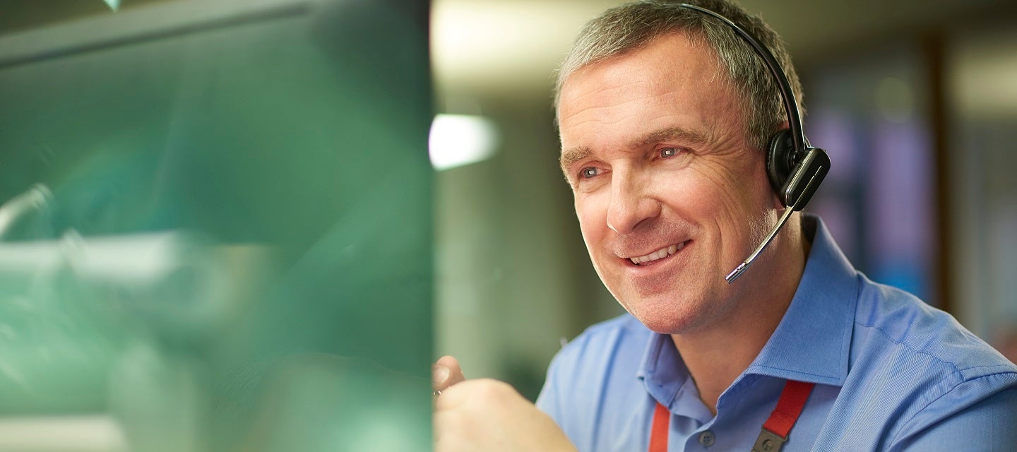 A man smiling while wearing a headset speaking to a customer over the phone