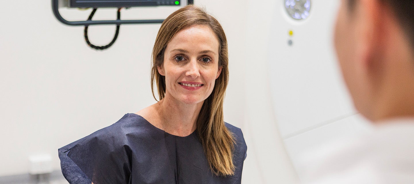 A female patient in a surgical gown preparing to have an MRI scan at I-MED Radiology
