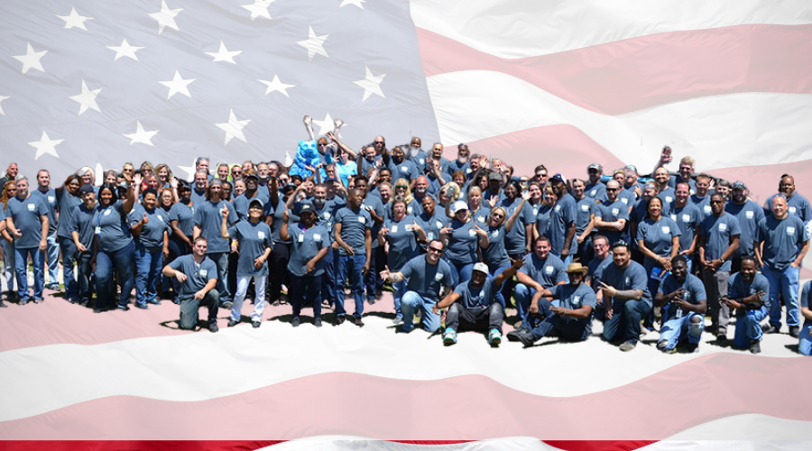 A large group of employees wearing matching shirts, posing together in front of an American flag backdrop.